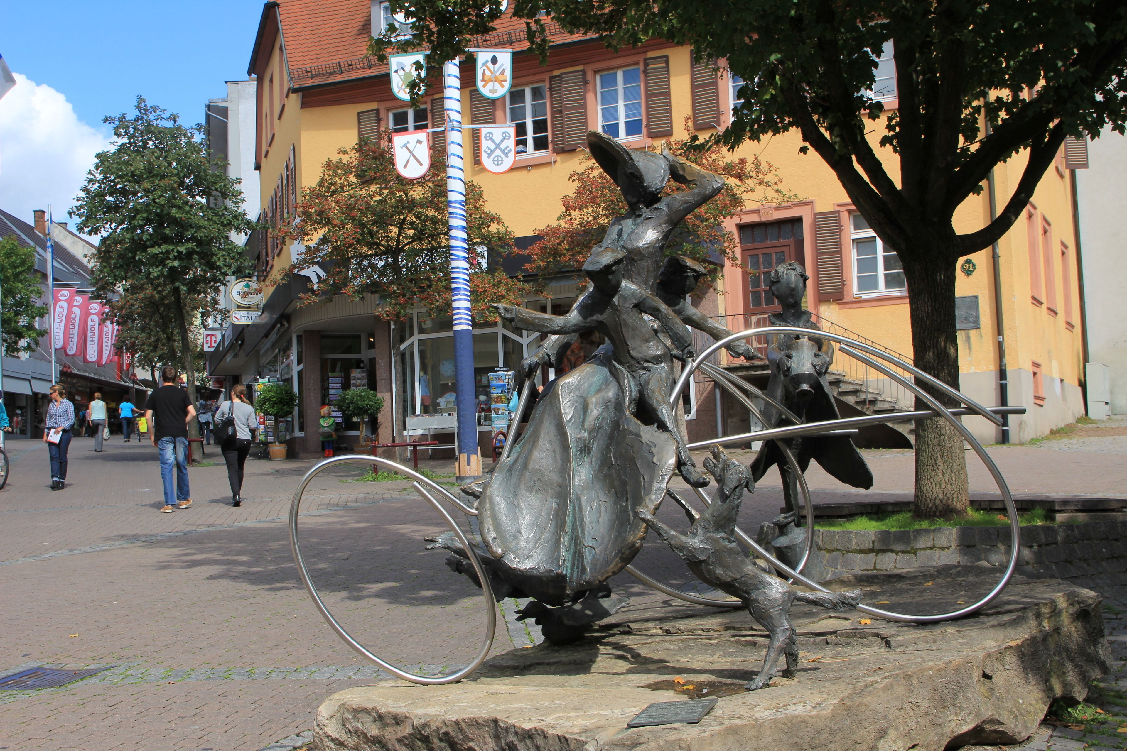 A sculpture of a horse and rider on a stone pedestal in a public square.