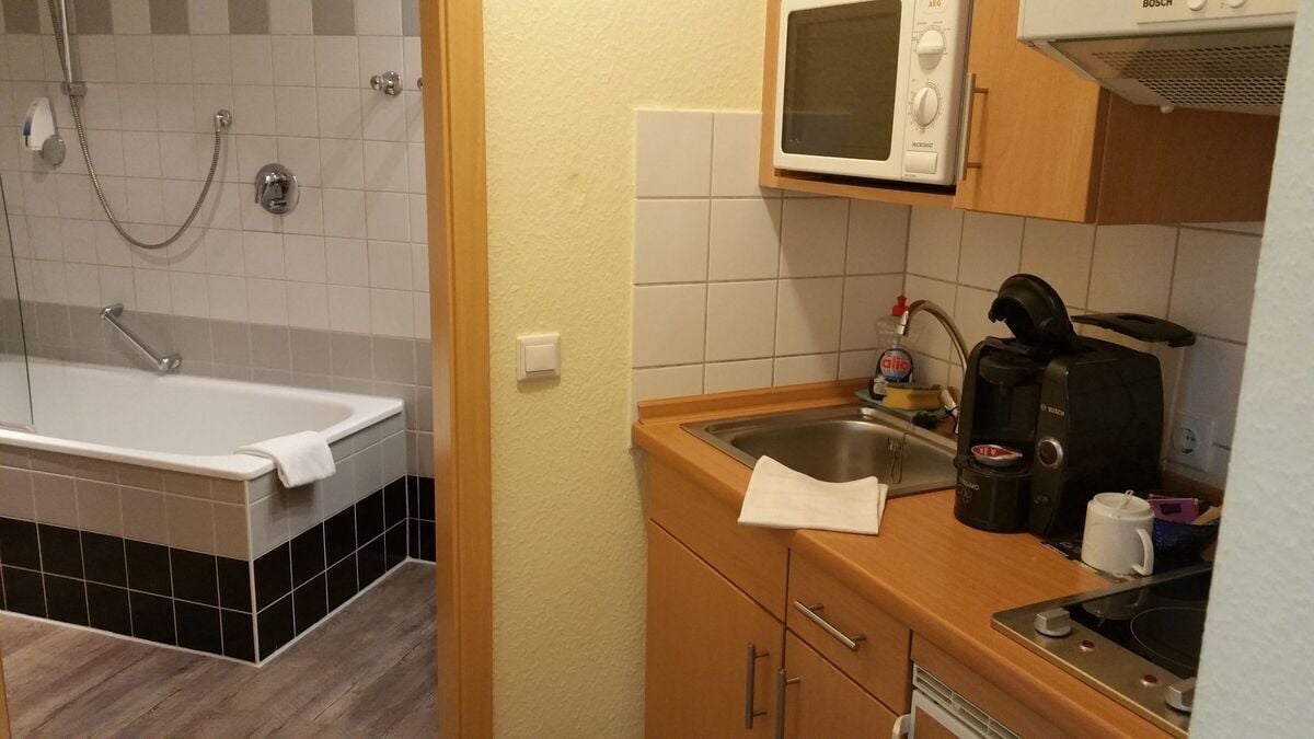 Ein Badezimmer mit einer Badewanne und einer Dusche, einem Waschbecken mit Kaffeemaschine und einer Mikrowelle über der Arbeitsplatte.