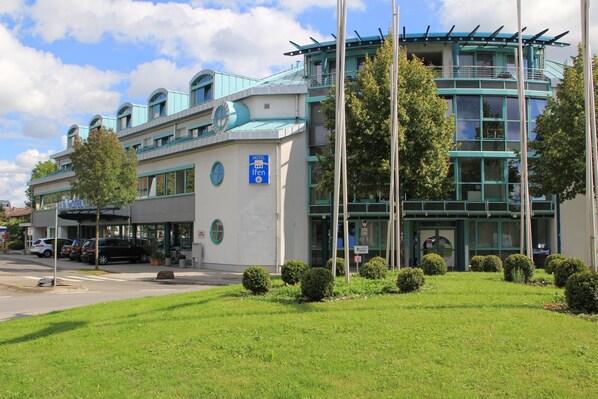 A hotel with a modern design, featuring a prominent glass facade and a rooftop terrace. - Hotel Ifen (Wiesloch)