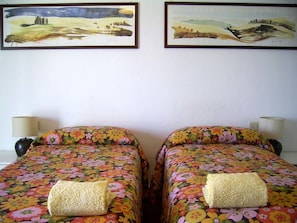 Dos camas individuales con ropa de cama floral, cada una con almohada a juego y lámparas de noche.