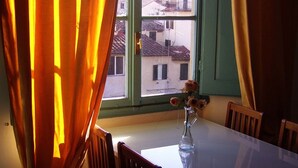Ein Esstisch mit Stühlen, eine Vase mit Blumen und ein Fenster mit Vorhängen.