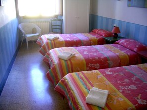 A room with three beds, each with colorful striped bedding and pillows, a white chair, and a small table with a lamp. - Locanda Daniel (Florence)