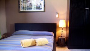 Ein Hotelzimmer mit einem Bett, einer Nachttischlampe, einem Stadtbild im Bilderrahmen und einer Tür.