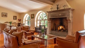 Un salón amplio con sofás de cuero, una chimenea y ventanas arqueadas grandes.
