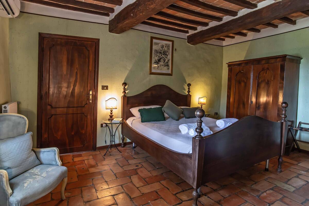 A bedroom with a wooden bed, a chair, a wardrobe, and a tiled floor.