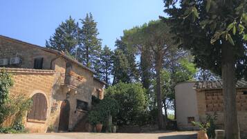 Un edificio rústico de piedra con ventanas arqueadas y una puerta, rodeado de árboles y un cielo despejado.
