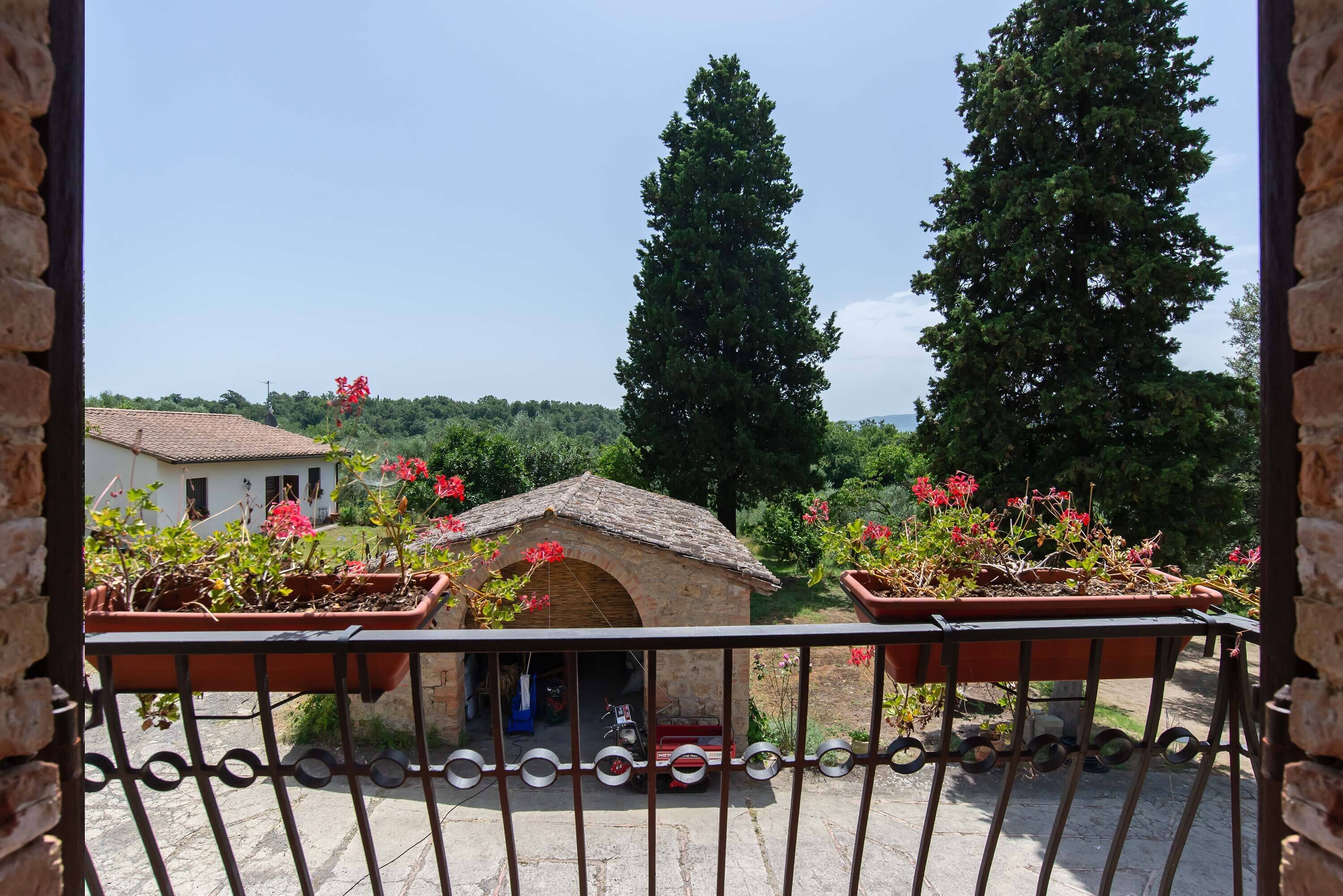 Un balcone con un muro in pietra, piante in vaso e vista su un paesaggio rurale con alberi e un edificio.