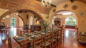 Un comedor espacioso con una larga mesa de madera dispuesta para una comida, rodeado de arcos de ladrillo y una araña.
