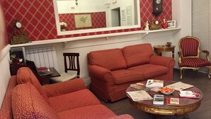 A living room with a red patterned sofa, a round coffee table with magazines, a wooden chair, and a mirror above a fireplace. - GH Casa Vicenza (Rome)