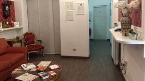 A room with a red armchair, a wooden coffee table with books, a red and gold chair, a vase with white flowers, and a blue door in the background. - GH Casa Vicenza (Rome)