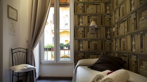 A hotel room with a bed, a chair, a bookshelf, and a window with curtains. - GH Casa Vicenza (Rome)