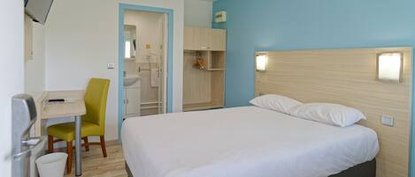 Habitación de hotel con cama, escritorio, silla, televisión y baño visible a través de una puerta abierta.