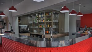 Un área de bar moderna con una barra de ladrillo rojo, estantes llenos de diferentes botellas e iluminación colgante roja.