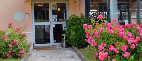 A hotel entrance with a stone pathway leading to the door, surrounded by pink flowers.