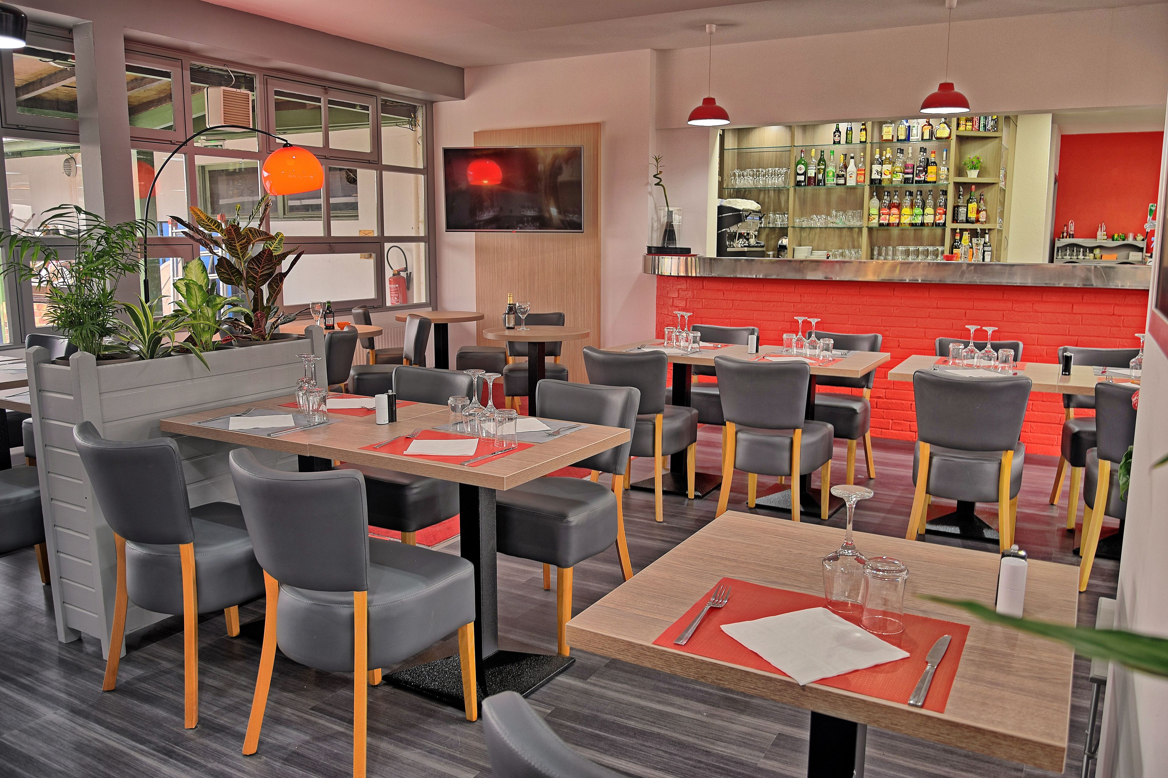 A modern restaurant with multiple tables and chairs, a bar area with shelves of bottles, and a large window with a view.