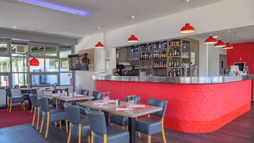 A modern restaurant with a red brick bar area, multiple seating tables with chairs, and a large window providing natural light.