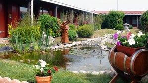 Un jardín con un estanque, un molino de madera y macetas con flores.