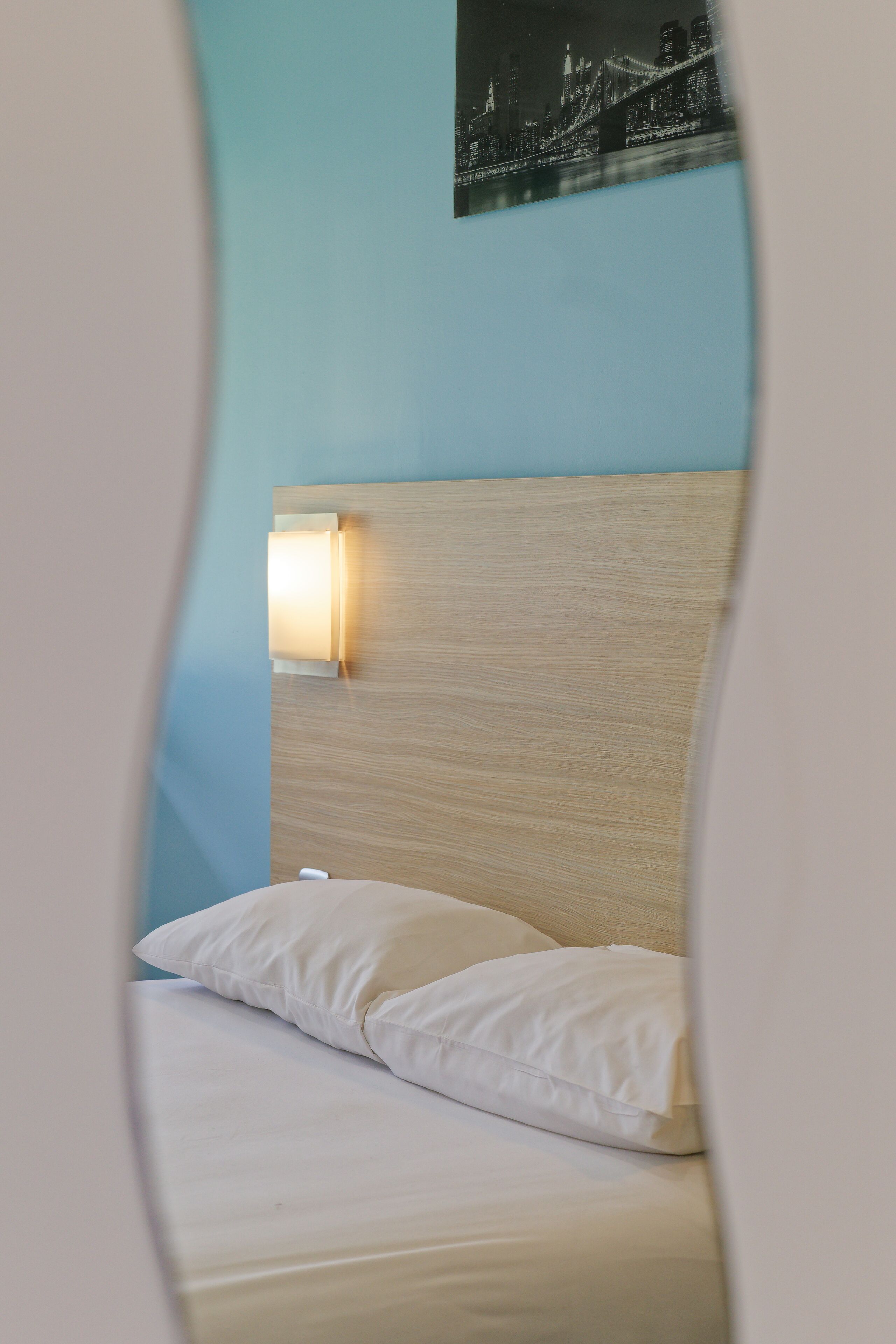 A bed with white bedding and pillows, a wooden headboard, and a wall-mounted light fixture.