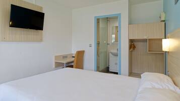 A hotel room with a bed, a desk, a chair, a TV mounted on the wall, and a bathroom visible through an open door.