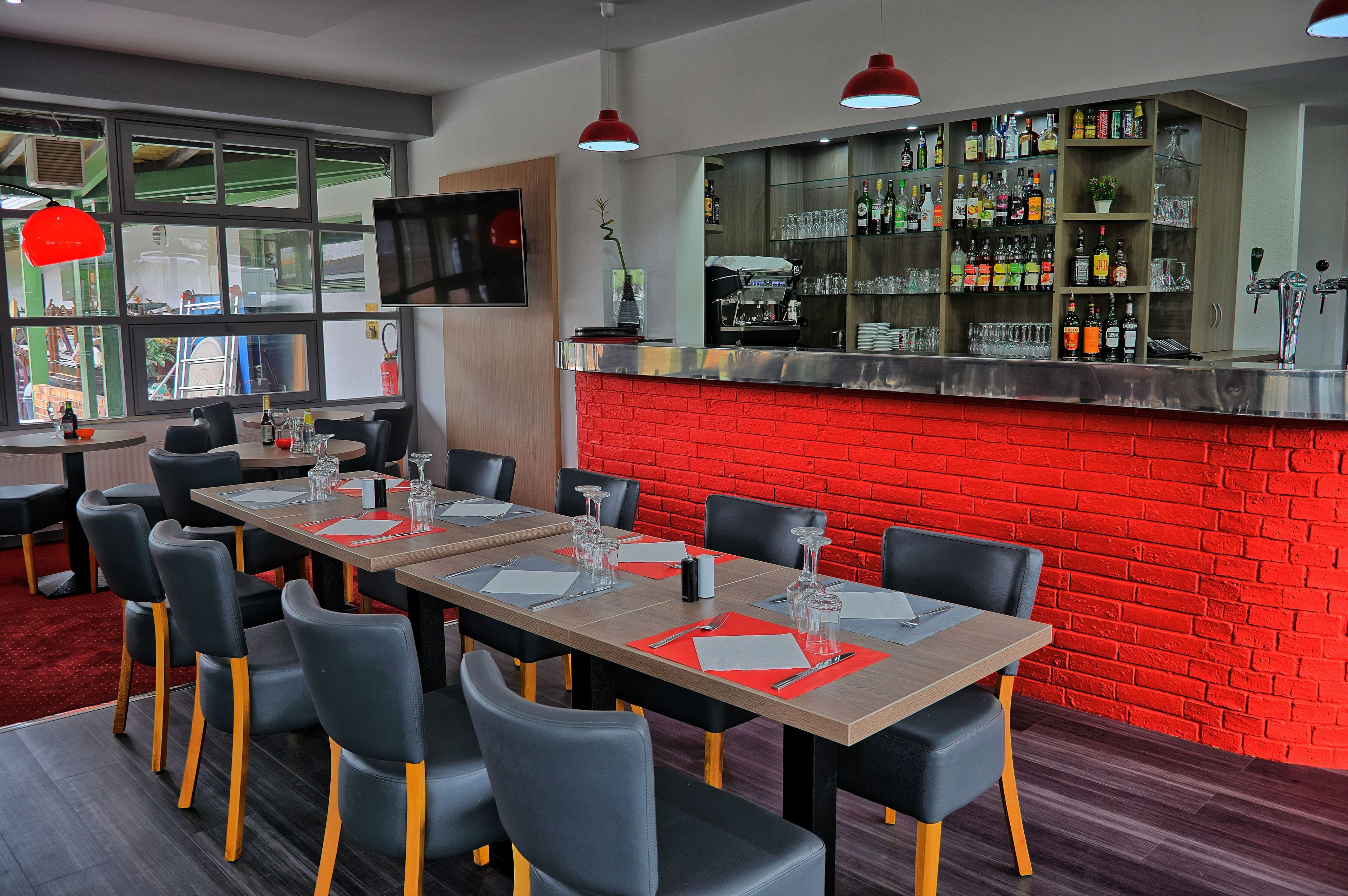 A modern restaurant with a red brick wall, a bar area with various bottles, and a seating area with tables and chairs.