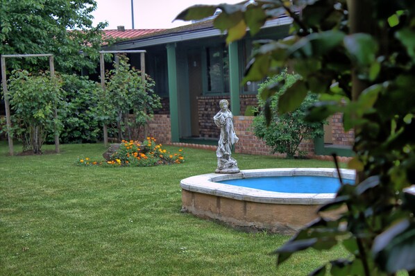 Un jardín con una estatua, piscina y un edificio de ladrillo con techo verde.