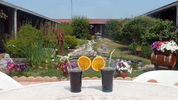 Un jardín con un estanque, dos bebidas con rodajas de naranja y una estructura de madera rústica.