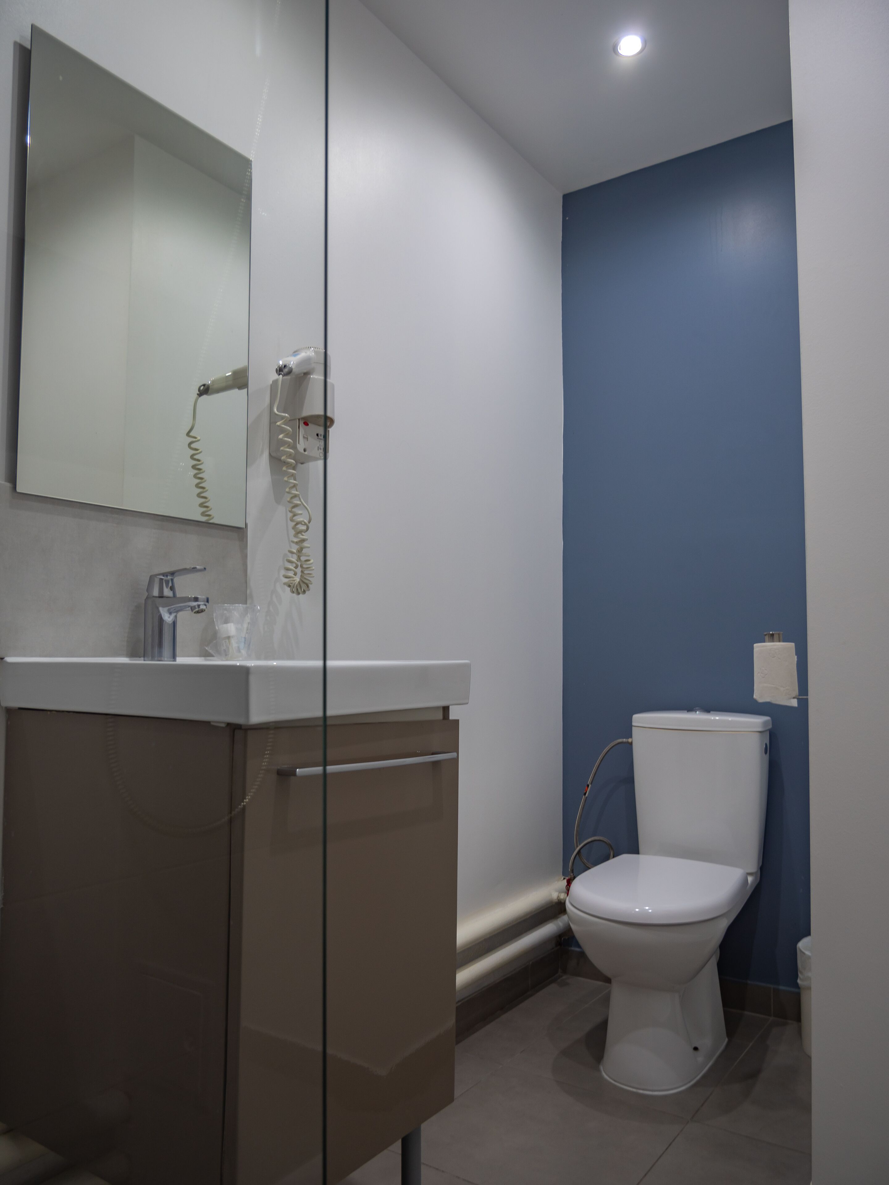 Une salle de bain avec un lavabo blanc, une douche en verre, des toilettes blanches et un mur d’accent bleu.