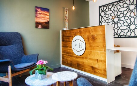 A reception area with a wooden reception desk, a blue chair, a small table with a vase of flowers, and a wall-mounted sign with 'VH'.
