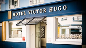 The exterior of Hotel Victor Hugo with a blue facade, a glass entrance, and a contact sign. - Victor Hugo (Lorient)