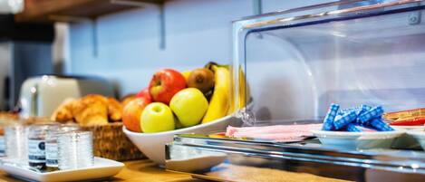 A breakfast buffet with fruits, pastries, and bottled water.