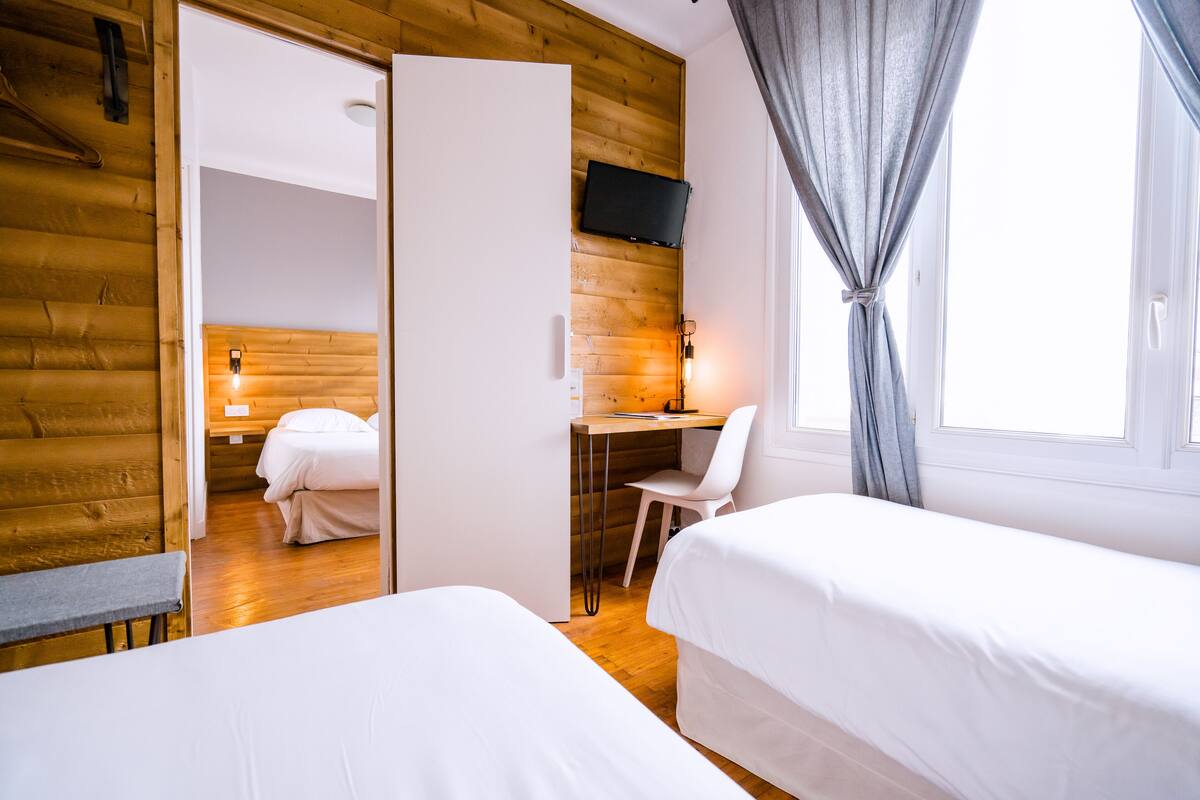 Una habitación con dos camas, un escritorio con silla, televisor en la pared y ventana con cortinas.