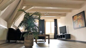 A living room with a large plant, a sofa, a TV, and a painting on the wall. - Hotel de Vischpoorte (Deventer)