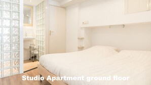 A studio apartment with a ground floor layout, including a bed, a small bathroom with a sink, and a glass partition wall. - Hotel de Vischpoorte (Deventer)