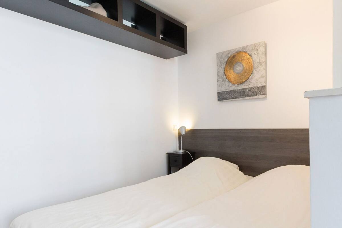 Une chambre à coucher comprenant un lit, une table de chevet avec une lampe, une étagère fixée au mur et une œuvre d’art décorative.
