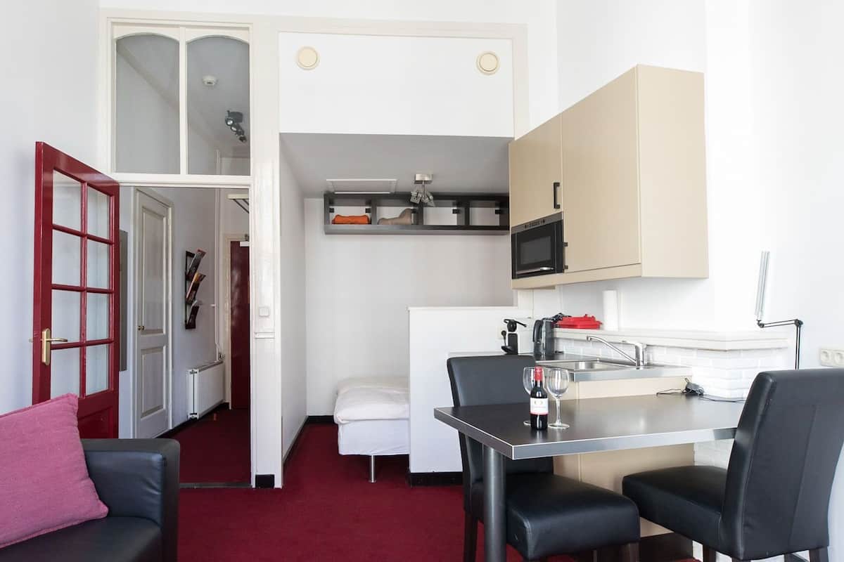 Un espace de vie compact comprenant un coin repas, une kitchenette et un petit coin salon avec un coussin rouge.