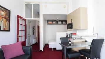 A compact living space with a dining area, kitchenette, and a small seating area with a red cushion.