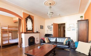 A living room with a fireplace, a leather sofa, a wooden coffee table, a chandelier, and a bunk bed in the background. - Hotel de Vischpoorte (Deventer)