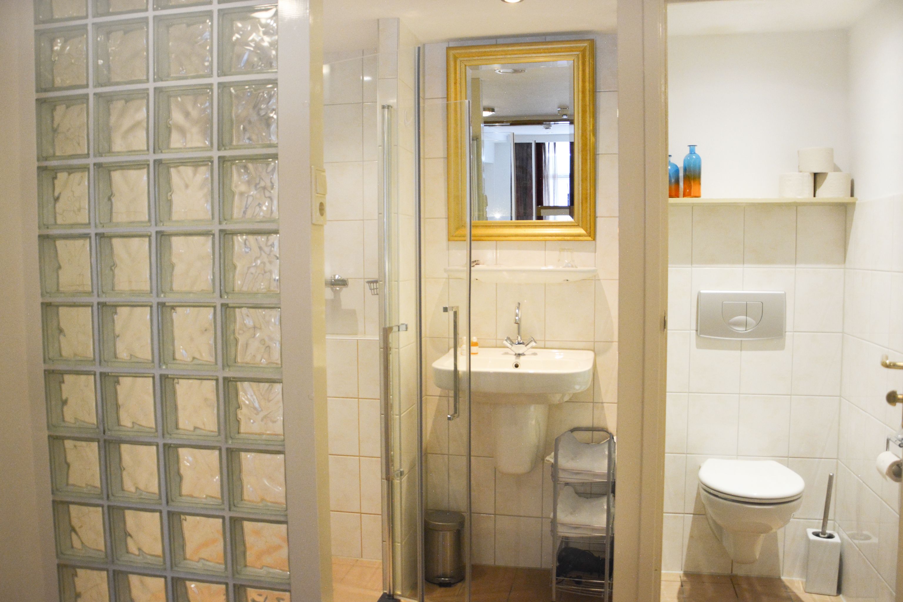 Un bagno con cabina doccia in vetro, lavandino, toilette e specchio con cornice dorata.