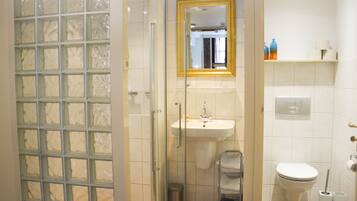 Un bagno con cabina doccia in vetro, lavandino, toilette e specchio con cornice dorata.