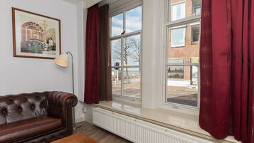 Een kamer met een bruine leren bank, een houten salontafel, een vloerlamp en een raam met rode gordijnen.