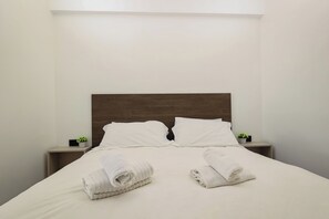 A neatly made bed with white linens and two towels, a wooden headboard, and small potted plants on bedside tables. - Seven Kings Relais (Rome)