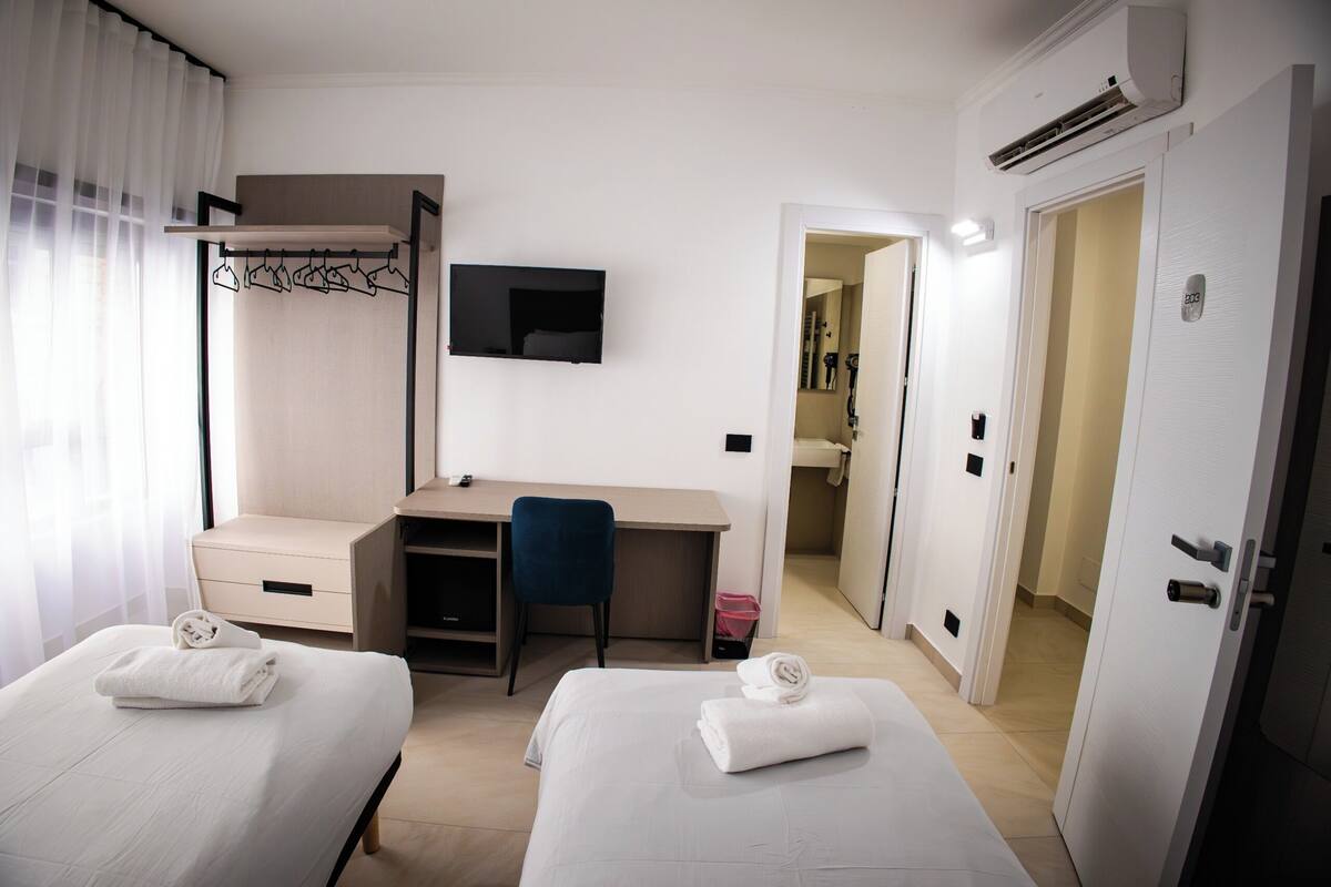 A hotel room with two beds, a desk, a chair, a TV, and a wardrobe.