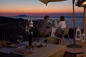 Un couple est assis à une table, profitant de la vue sur le coucher de soleil et les montagnes.