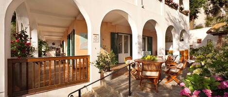 A courtyard with stone flooring, wooden furniture, and potted plants.