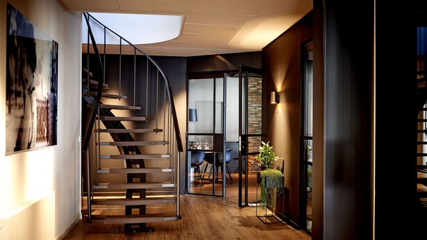 A modern interior with a spiral staircase, wooden flooring, and a glass door leading to a dining area.