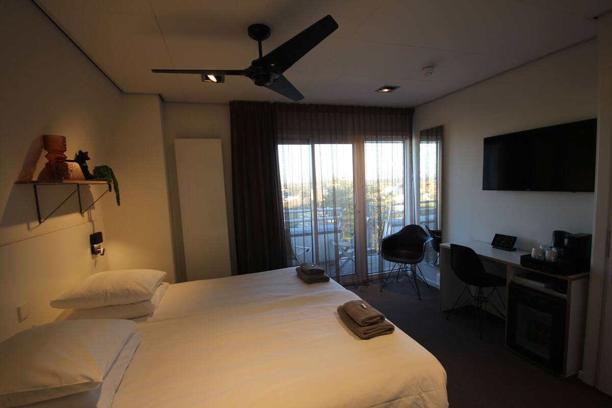 A hotel room with a bed, a desk, a chair, a television, and a balcony with a view.
