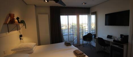 Une chambre d’hôtel équipée d’un lit, d’un bureau, d’une chaise, d’une télévision et d’un balcon avec vue.
