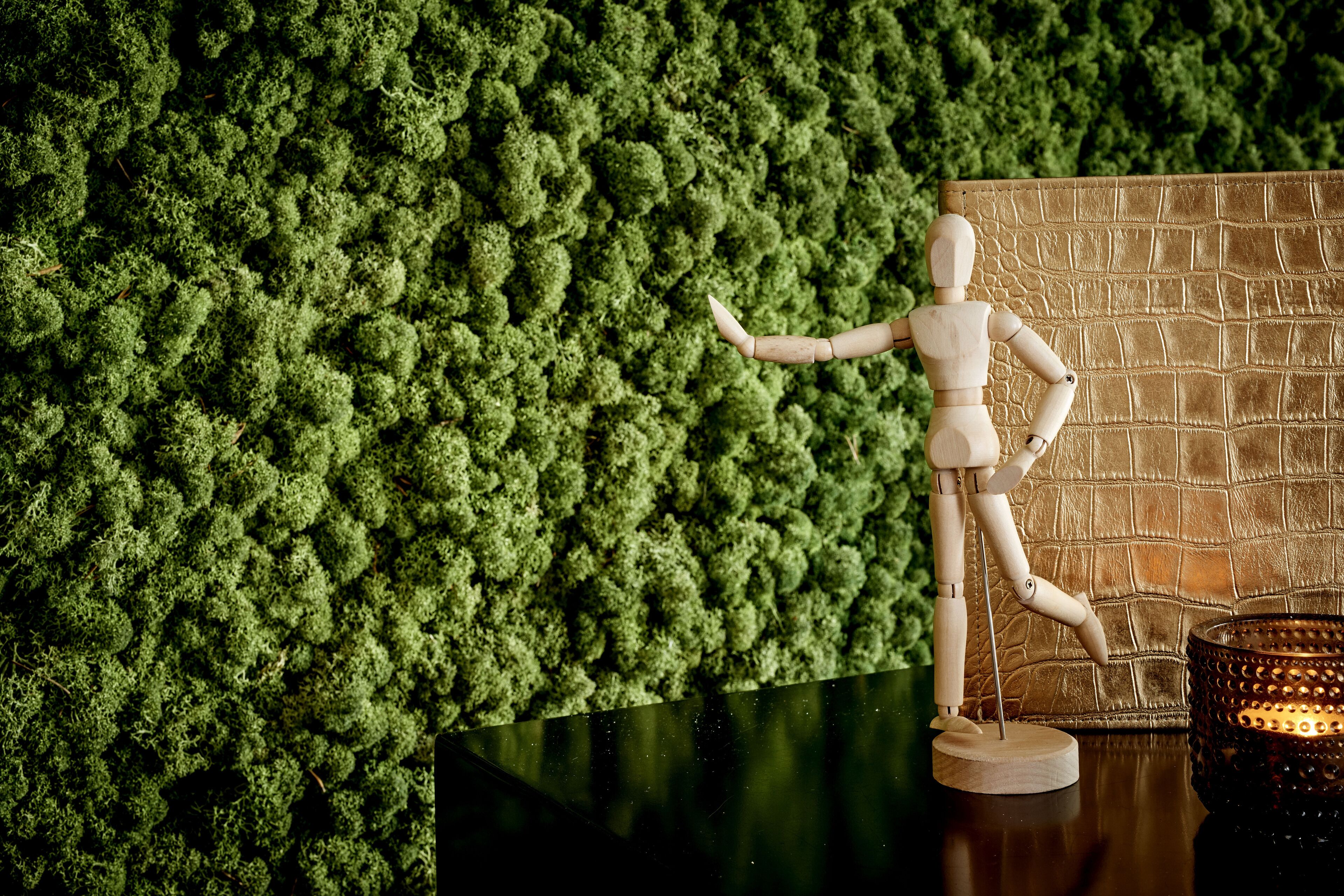 A wooden mannequin on a black surface with a textured wall and a textured brown panel in the background.