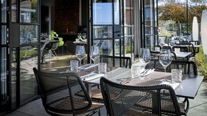 An outdoor dining area with tables and chairs, glassware, and a view of the surrounding area.