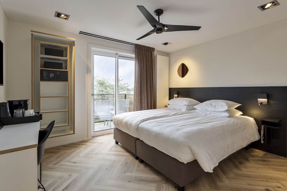 A modern hotel room with a large bed, a desk with a coffee machine, a ceiling fan, and a view of the outdoors.